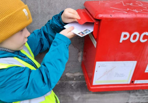 chłopiec wrzuca list do czerwonej skrzynki pocztowej