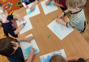 Dzieci malują kartkę na kolor niebieski.