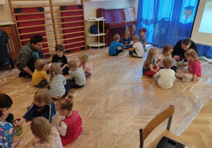 Dzieci siedzą w grupach na podłodze i mieszają farby.