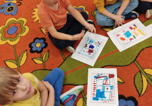 Dzieci na dywanie demonstrują swoje prace.