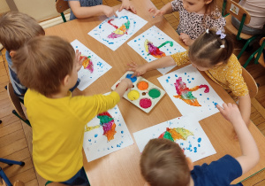 Dzieci farbami malują parasolki.
