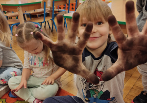 Chłopiec pokazuje ubrudzone ręce węglem.
