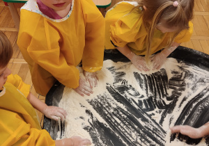 Dzieci ugniatają, dzielą, przesypują mąkę palcami.