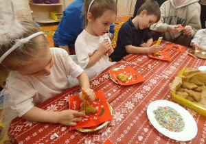 Dzieci przy stole dekorują pierniki.