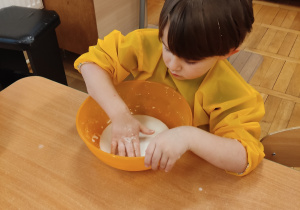 Chłopiec bawi się substancją powstałą z połączenia wody i mąki.