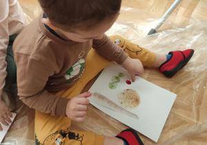 Chłopiec przykleja owoce i warzywa na kartkę.