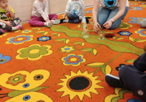 Dzieci wraz z nauczyciele siedzą na dywanie.