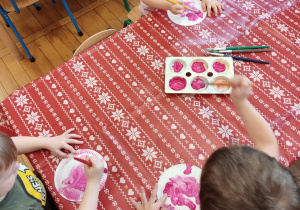 Dzieci malują różową farbą talerzyki.