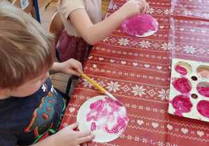 Dzieci malują papierowy talerzyk na różowo.