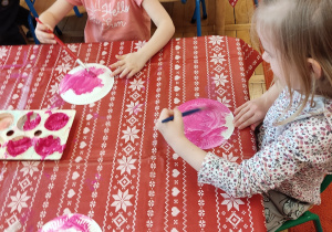 Dzieci malują talerzyki różową farbą.