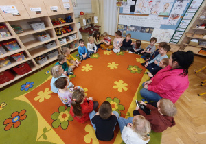 Na zdjęciu widać grupę dzieci siedzącą w kręgu razem z nauczycielem