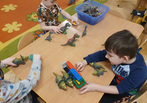 Na zdjęciu chłopcy bawią się figurkami dinozaurów
