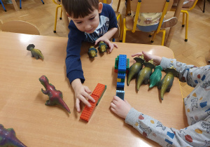 Na zdjęciu chłopcy bawią się figurkami dinozaurów