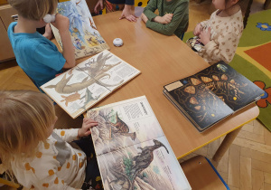 Na zdjęciu dzieci oglądają albumy ze zdjęciami dinozaurów.