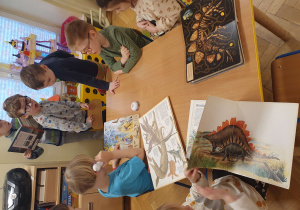 Na zdjęciu dzieci oglądają albumy ze zdjęciami dinozaurów