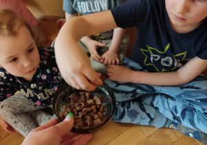 Dzieci częstują się kawałkiem czekolady.