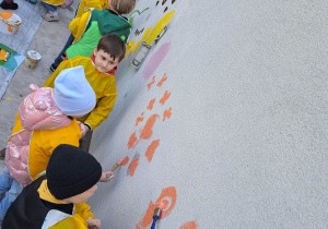 Dzieci malują budynek przedszkola.
