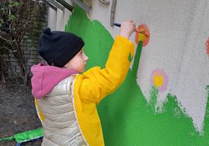 Dziewczynka maluje budynek przedszkola.