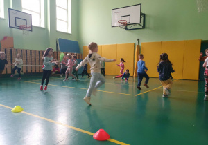 Na zdjęciu widać dzieci na sali gimnastycznej uczestniczące w zajęciach sportowych