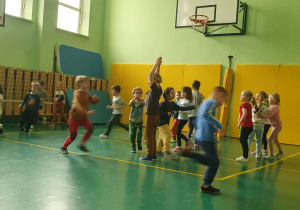 Na zdjęciu widać dzieci na sali gimnastycznej uczestniczące w zajęciach sportowych