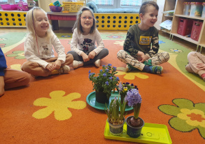 Dzieci na zdjęciu zapoznają się z roślinami, kwiatami zwiastującymi pierwsze oznaki wiosny