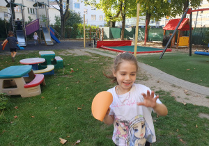 Na zdjęciu dziewczynka biegnie z papierową kropką w dłoni znalezioną na placu zabaw