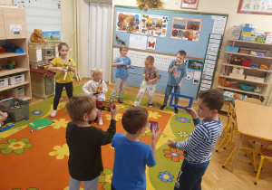 Na zdjęciu widać dzieci, które udają, że grają na instrumentach zrobionych z klocków. Inne dzieci mają z klocków zrobione kamery i bawią się w nagrywanie koncertu.
