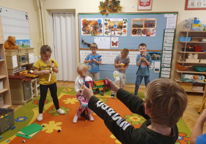 Na zdjęciu widać dzieci, które udają, że grają na instrumentach zrobionych z klocków. Jeden chłopiec udaje, że nagrywa kamerą z klocków.