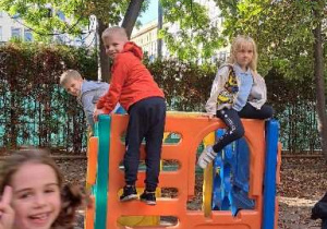 Na zdjęciu chłopiec wspina się po budowli zabawkowego domku w ogrodzie przedszkolnym.