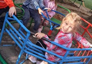 Na zdjęciu dzieci w ogrodzie przedszkolnym kręcą się na małej karuzeli.