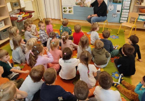 Na zdjęciu widać dzieci słuchające jak nauczycielka czyta im książkę.