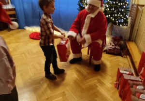 Święty Mikołaj rozdaje dzieciom prezenty.