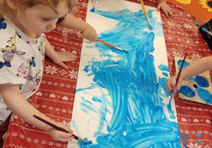 Dzieci malują kartkę na niebiesko