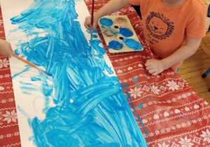 Dzieci malują kartkę na niebiesko
