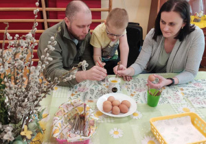 Rodzice wraz z synem dekorują jajko.