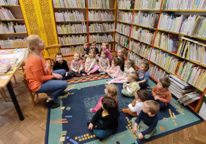 Dzieci siedzą na dywanie w bibliotece.