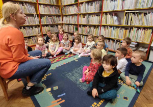 Dzieci siedzą na dywanie w bibliotece.