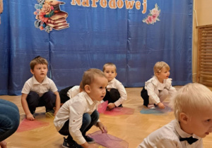 Dzieci na przedszkolnej scenie prezentują układ taneczny z kolorowymi chustami.