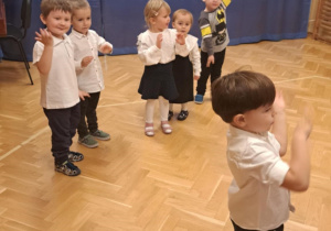 Dzieci na przedszkolnej scenie prezentują układ taneczny do piosenki