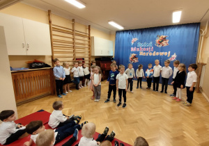 Dzieci stoją na przedszkolnej scenie w półkolu i cytują wierszyki