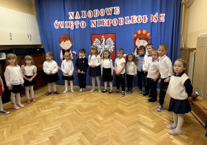 Dzieci stoją na przedszkolnej scenie i śpiewają hymn