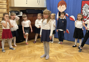 Dzieci stoją na przedszkolnej scenie i prezentują wiersze i piosenki