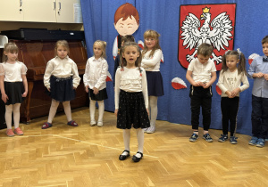 Dzieci stoją na przedszkolnej scenie i prezentują wiersze i piosenki