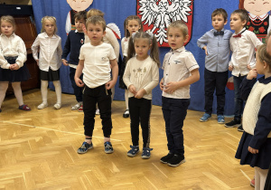 Dzieci stoją na przedszkolnej scenie i prezentują wiersze i piosenki