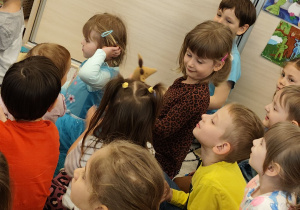 Dzieci siedzą na dywanie i oglądają maskotki.