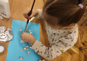 Dziewczynka przykleja folię aluminiową na kartkę.