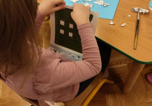 Dziewczynka składa okienko z kartonu.