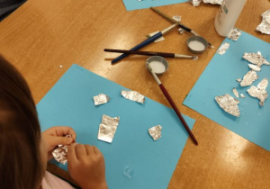 Dziewczynka przykleja folię aluminiową na kartkę.