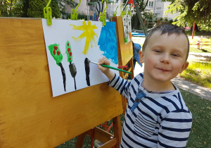 Chłopiec maluje farbami obraz.
