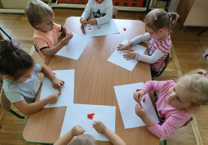 Dzieci wykonują pracę plastyczną przy stoliku.